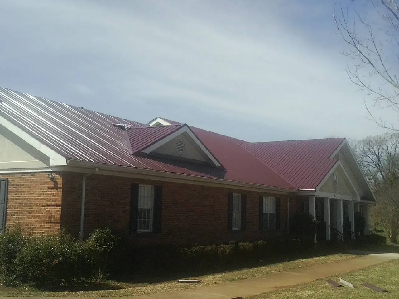 Red metal roof with gabled entries on a long brick building, from a Hail Damage Roof Repair job in Lambertville