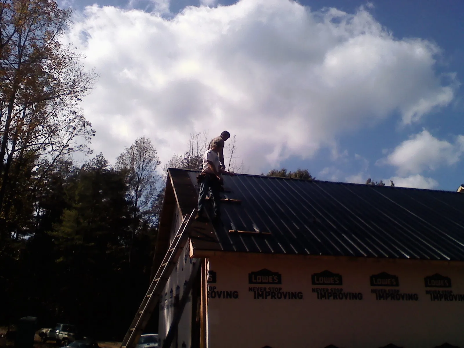 Roofer fastening dark metal panels high against a cloudy sky, from a Roof Inspection job in Lambertville