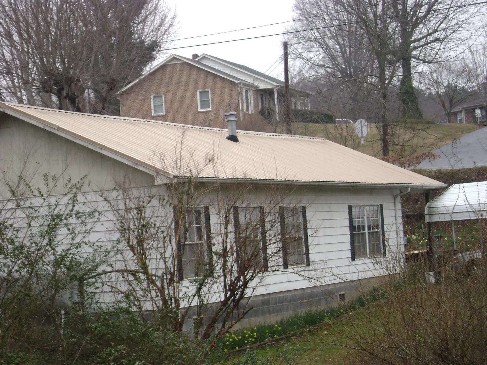 Tan metal roof on a white sided house set into a hillside — Commercial Roofing by Roofing Brothers in Lambertville